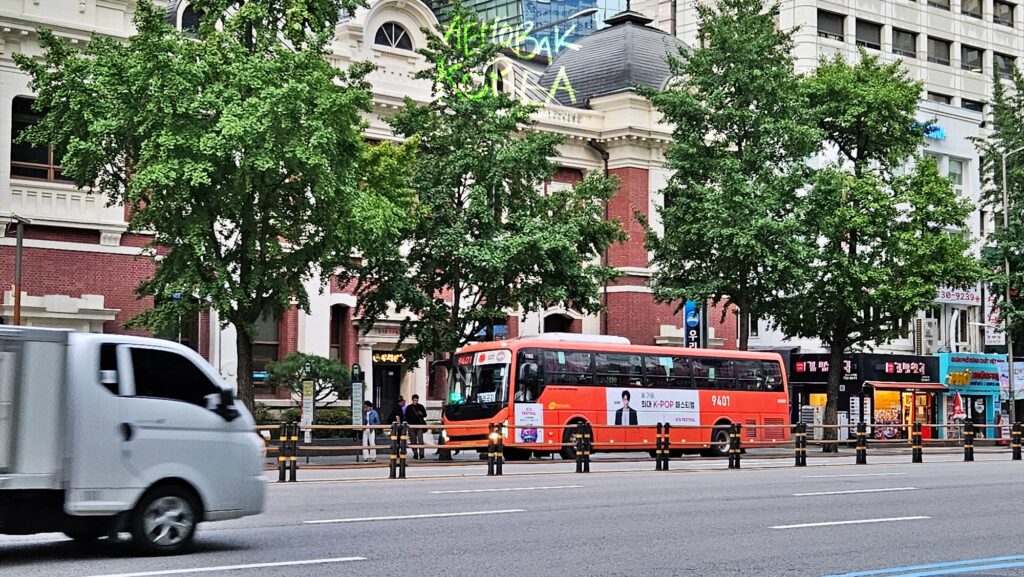 Red express bus driving on main street in central Seoul near old building