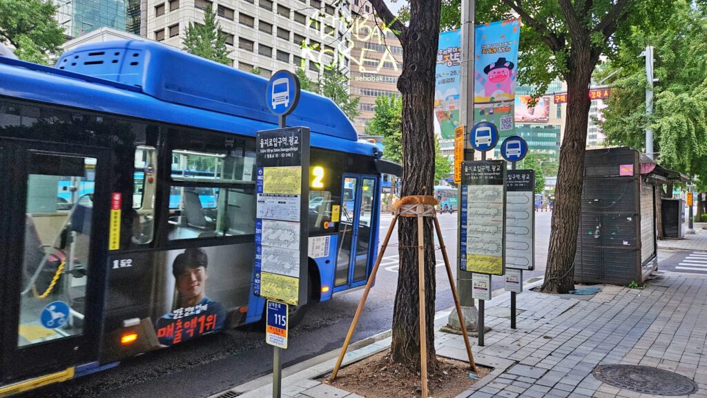 Blue city bus leaving Euljiro bus stop in Seoul with clear route signs and maps